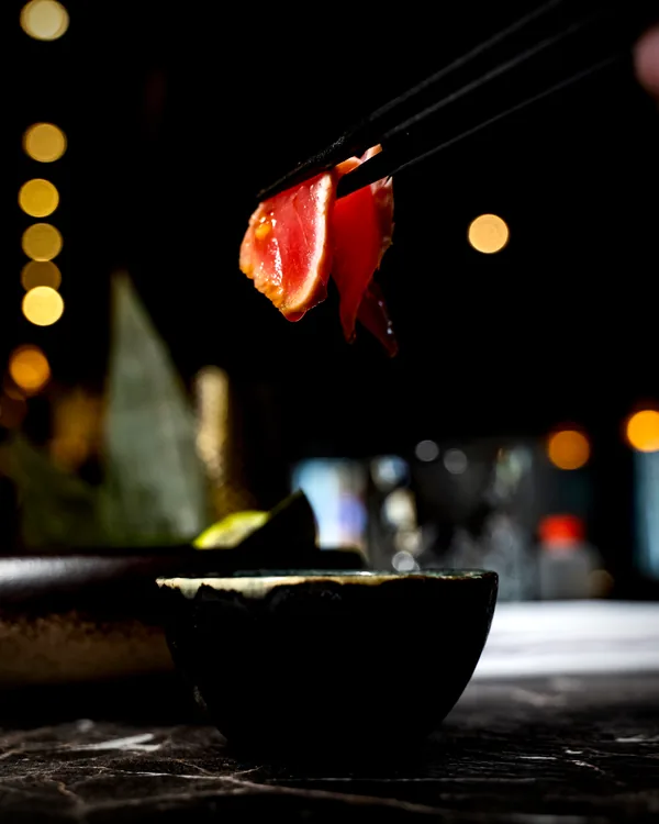 Tonijnsashimi aan stokjes boven een schaaltje bij kaarslicht